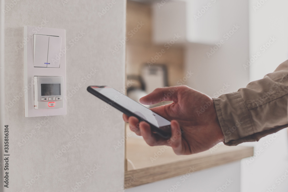 Smartphone connecting to floor heating controller in kitchen. Remote home control system on a smartphone.