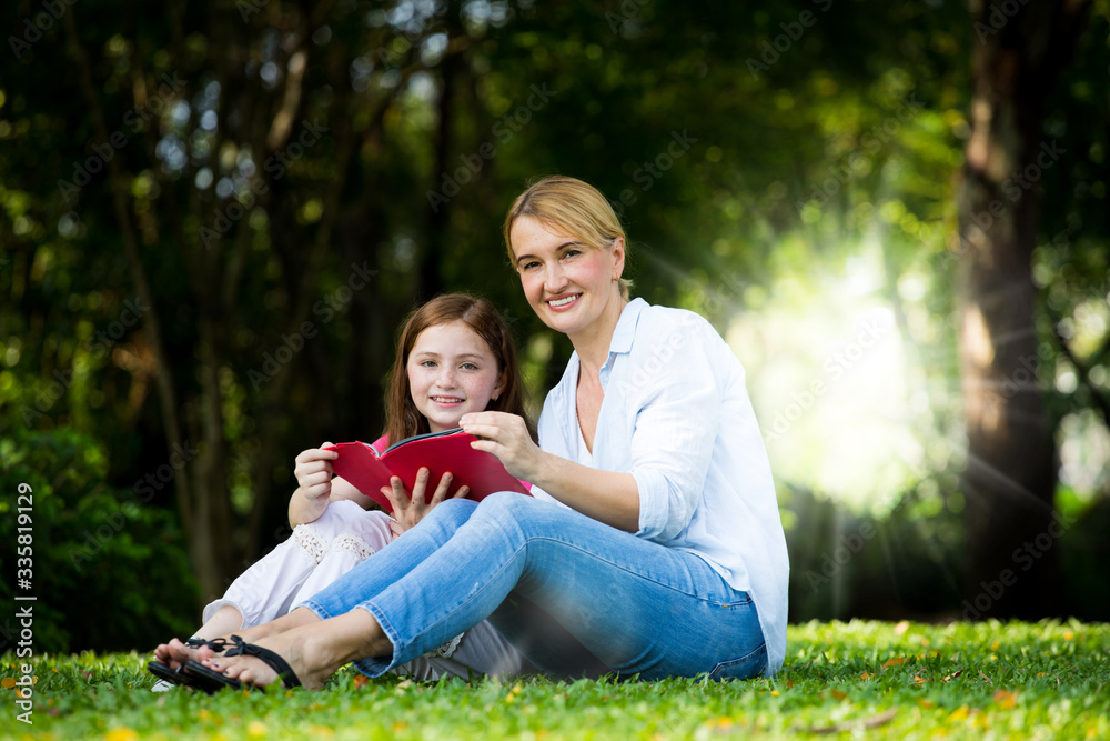 beautyful Mother and cute daughter are reading a book and smile at the park . Happiness and harmony in family life concept. beautyful Mother and cute daughter are reading a book and smile at the park . Happiness and harmony in family life concept.
