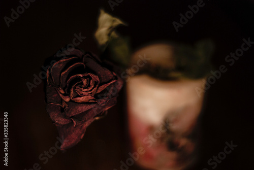 Φωτογραφία Withered red rose in the focused foreground and a scented candle in the out of focus backdrop in a low key composition
