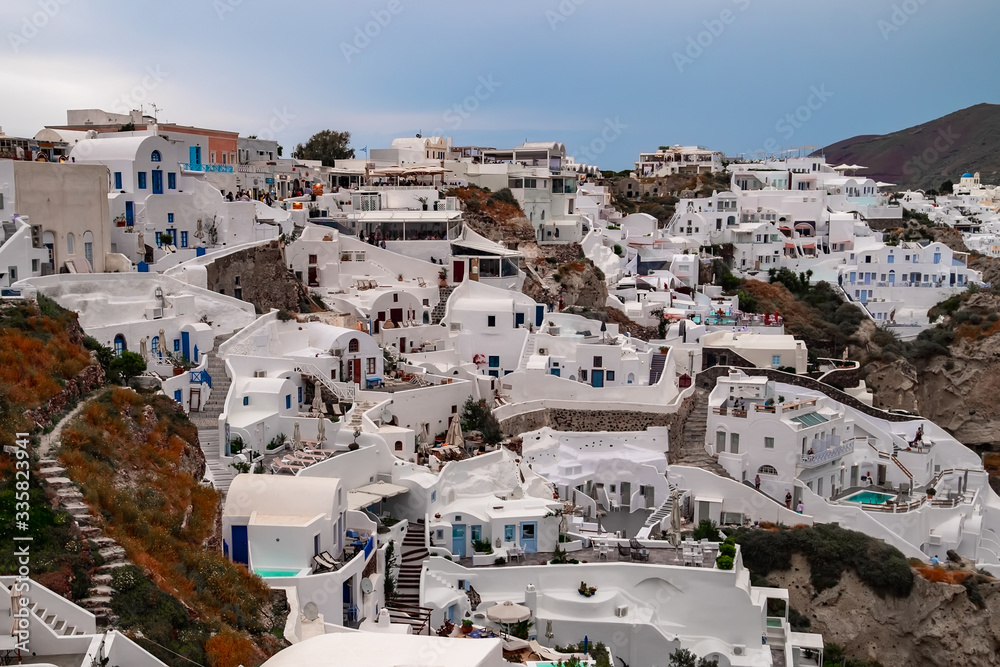 Fototapeta premium Oia town on Santorini island. Old fishing village on hill slope. Romantic honeymoon in beautiful touristic resorts. Amazing white houses on volcanic rocks. Popular landmark in Europe. Greece