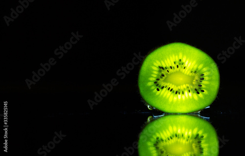 Kiwi illuminated by a flashlight on the mirror 

Photo taken at home, 4.04.2020, fruit, mirror, disk, water 