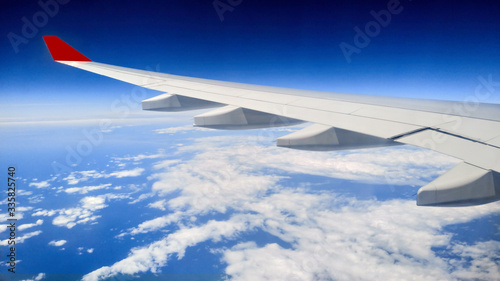 Wing of an airplane flying above in the morning with blue sky and clouds background.