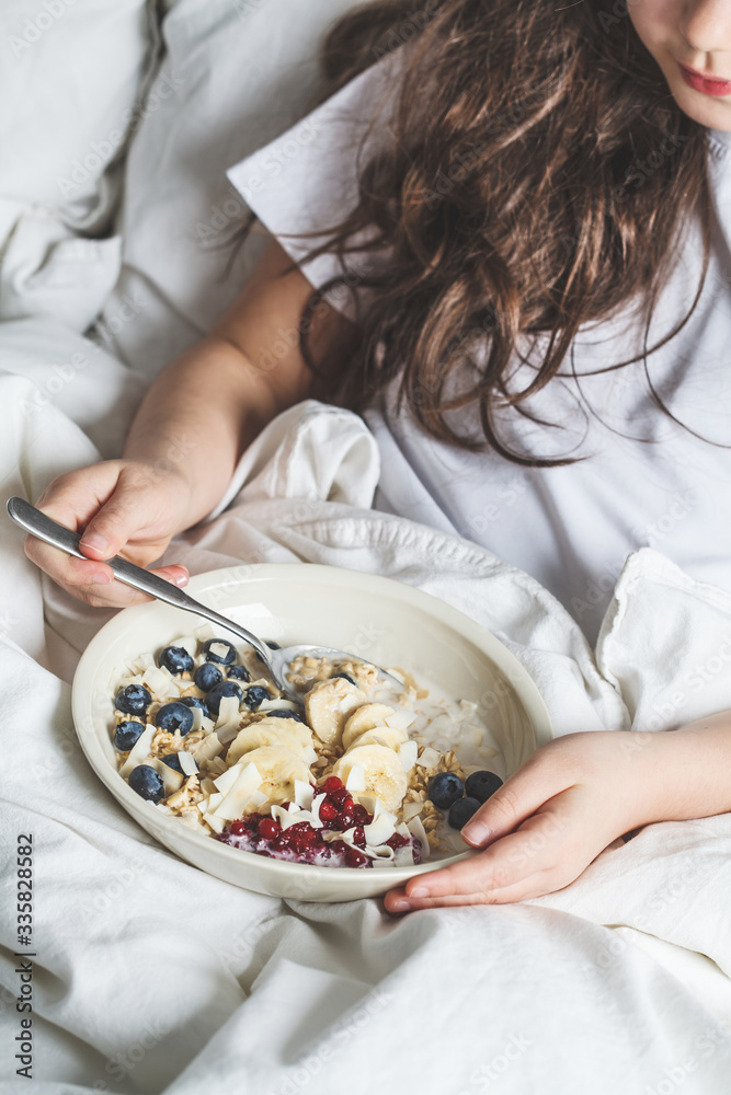 Beautiful little girl eating healthy oatmeal with fruits and berries in white bed. Beautiful little girl eating healthy oatmeal with fruits and berries in white bed.