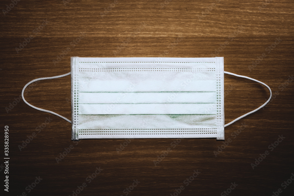 a medical mask on a wooden background. advice for the public to wear face masks to protect the respiratory system from coronavirus disease (COVID-19). a medical mask on a wooden background. advice for the public to wear face masks to protect the respiratory system from coronavirus disease (COVID-19).
