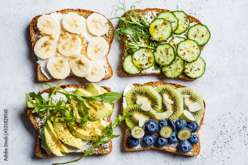 Breakfast toasts with various healthy toppings. Sandwiches with cream cheese, fruits, berries and honey, salted toasts with avocado and cucumber, top view.
