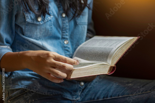 Young woman sitting outdoor and  reading bible book with phone on the table, garden nature background. Education concept. photo