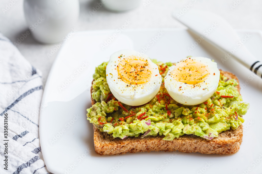Breakfast avocado toast with egg on a white plate.