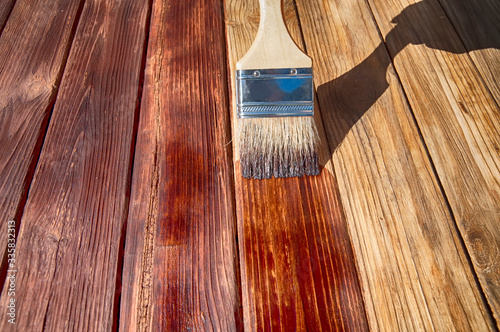 a wooden brush covers the wooden plank surface with a dark red stain front side view close up