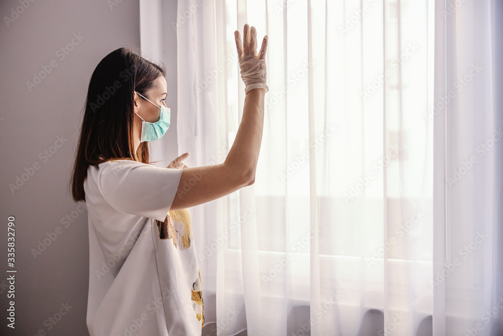 Young woman with face mask and gloves looking trough the window. Feeling lonely during isolation. Quarantine melancholy. Stay at home. Young woman with face mask and gloves looking trough the window. Feeling lonely during isolation. Quarantine melancholy. Stay at home.