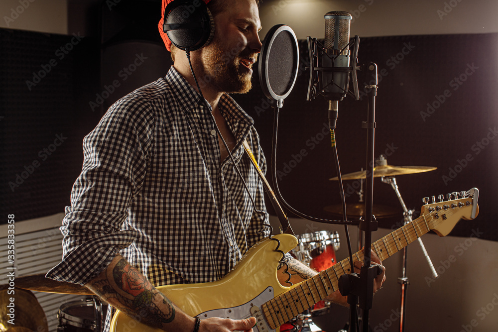 Fototapeta premium awesome caucasian musician play electric guitar and sing in recording studio. man preparing, practicing before music performance, before concert. music, instruments concept