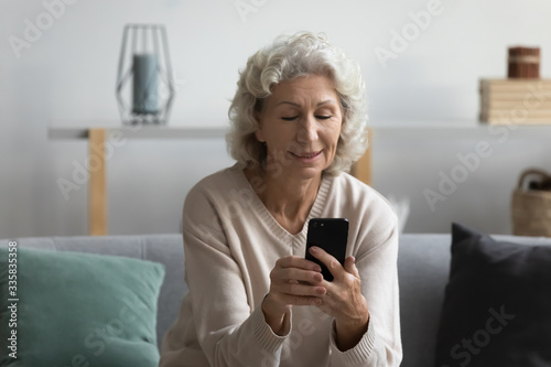 Satisfied smiling positive middle aged woman resting on comfortable couch, using mobile applications, chatting with friends in social networks, reading news in media, shopping online alone at home.