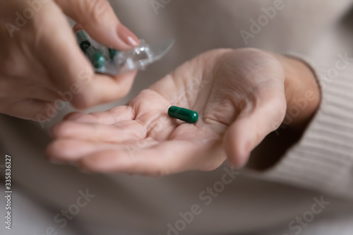 Close up middle aged woman pouring capsule pills out of plastic blister. Elderly mature grandmother using painkillers reducing headache or taking daily dose of vitamins, retirement healthcare concept.