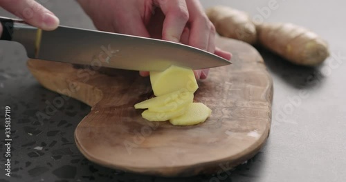 Slow motion man hands slicing fresh ginger root with knife on olive wood board photo