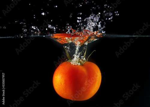 Falling tomato with a green tail into the water, spray for design, freezing in motion. Water splash and vegetables isolated on a black backgroud