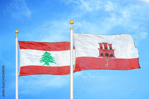 Lebanon and Gibraltar two flags on flagpoles and blue cloudy sky photo