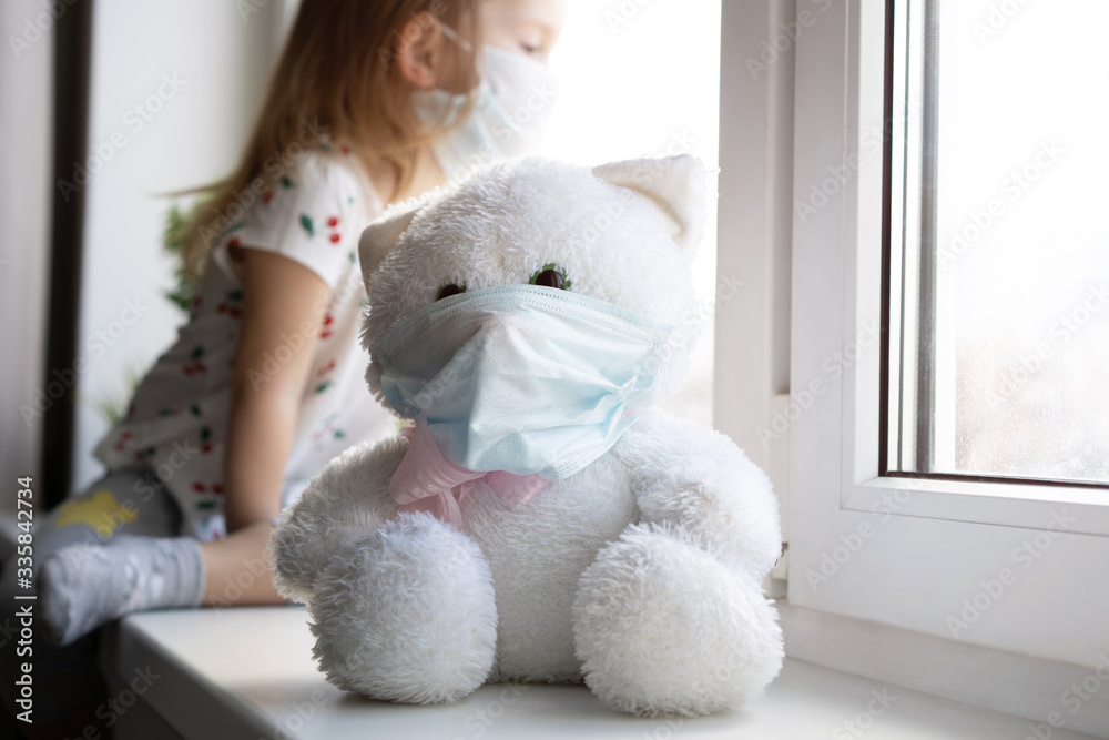 Sad child and his teddy bear both in protective medical masks. Children and illness COVID-2019 disease concept Sad child and his teddy bear both in protective medical masks. Children and illness COVID-2019 disease concept