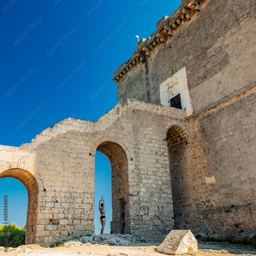 Nardò, Italy, Puglia, Salento. Torre dell'Alto, the watchtower of Porto Selvaggio. A beautiful girl in a black bikini, shot from behind, poses for the photo, under the arch of the staircase. Blue sky.