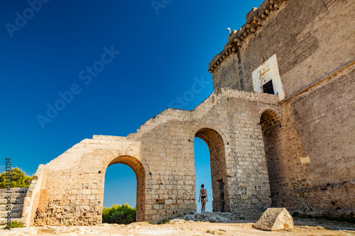 Nardò, Italy, Puglia, Salento. Torre dell'Alto, the watchtower of Porto Selvaggio. A beautiful girl in a black bikini, shot from behind, poses for the photo, under the arch of the staircase. Blue sky.