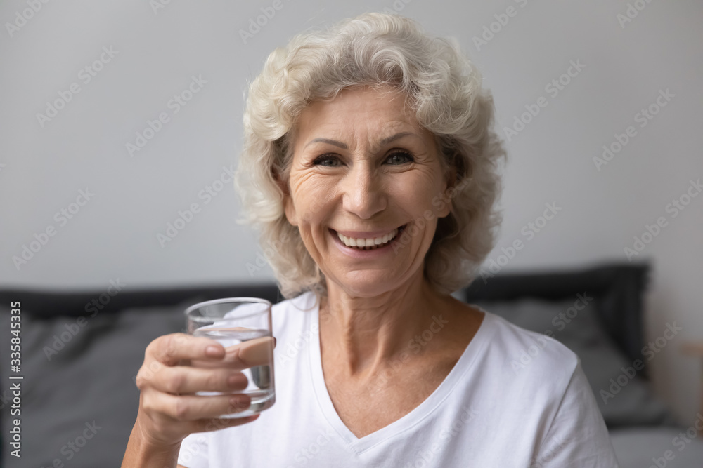 Head shot close up portrait happy senior elderly woman holding glass of fresh pure distilled water, looking at camera. Smiling middle aged grandmother enjoying healthy habit, drinking aqua every day. Head shot close up portrait happy senior elderly woman holding glass of fresh pure distilled water, looking at camera. Smiling middle aged grandmother enjoying healthy habit, drinking aqua every day.