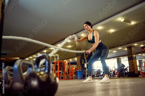Caucasian fit woman dressed in sportsoutfit doing workout with battle ropes at gym.