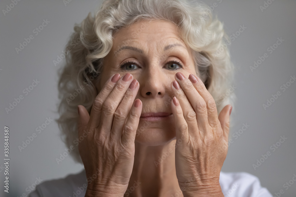 Beautiful elderly retired woman looking at camera, applying nourishing anti age cream on face, head shot close up. Attractive middle aged mature lady moisturizing skin, doing morning skincare routine. Beautiful elderly retired woman looking at camera, applying nourishing anti age cream on face, head shot close up. Attractive middle aged mature lady moisturizing skin, doing morning skincare routine.