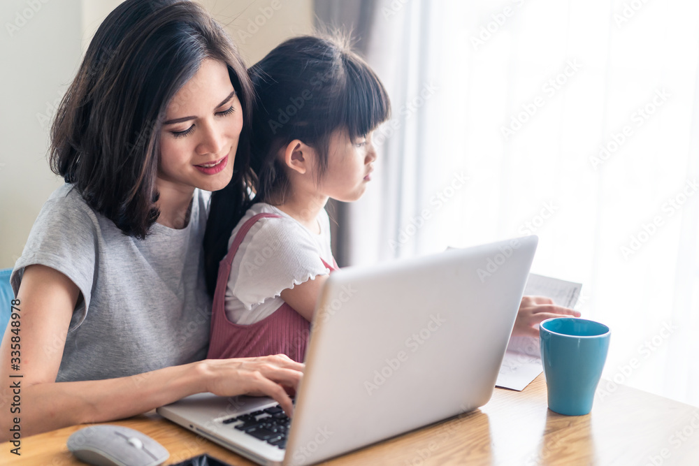 Asian young mother work from home. Woman use laptop for meeting with colleague while daughter sit on the lap and play. Mom happy to do job while taking care family. Covid-19, Social distancing concept Asian young mother work from home. Woman use laptop for meeting with colleague while daughter sit on the lap and play. Mom happy to do job while taking care family. Covid-19, Social distancing concept