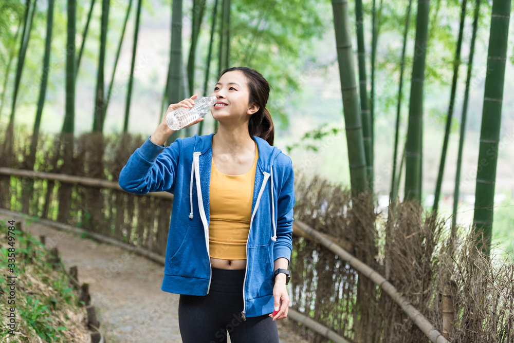 A young Asian woman resting and drinking water in a bamboo forest A young Asian woman resting and drinking water in a bamboo forest