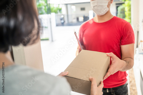 Asian postman or deliveryman carry small box deliver to young woman customer in front of door at home. Man wearing mask prevent covid or coranavirus affection outbreak. Social distancing work concept. photo