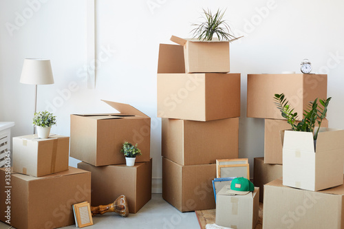 Background image of cardboard boxes stacked in empty room with plants and personal belongings inside, moving or relocation concept, copy space © Seventyfour