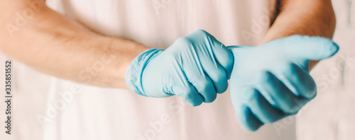 Banner closeup man wearing blue latex medical gloves on hands. Professional doctor putting on sterile protective gloves. Preparation for patient examination. Personal protection. Coronavirus COVID-19