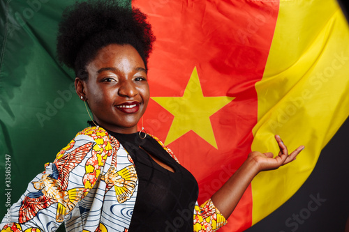 African woman in national clothes posing and dancing against flag of Cameroon