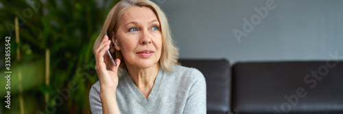 Beautiful mature blond woman talking on mobile phone at sofa.