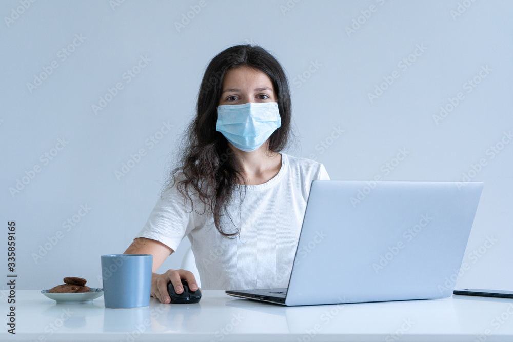 The girl works from home during quarantine. Corona virus pandemic. A girl in a surgical mask works on a laptop and drinks coffee. Distant work The girl works from home during quarantine. Corona virus pandemic. A girl in a surgical mask works on a laptop and drinks coffee. Distant work