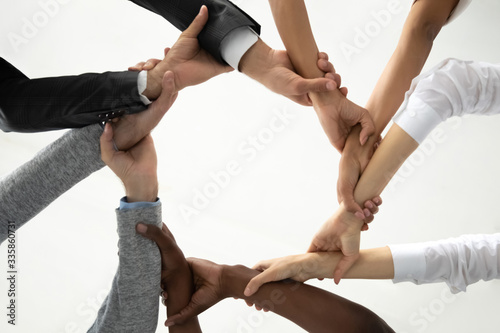 Close up bottom view concept of multiracial business people holding each others wrists, create hands circle. Support and unity team strength and power. Colleagues involved in team building activity.