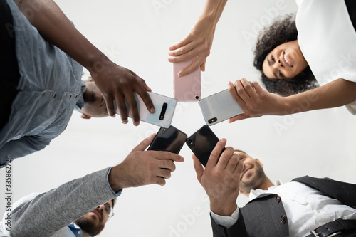 Fototapeta Naklejka Na Ścianę i Meble -  Close up diverse team employees using phones together bottom hands view. Colleagues holding smartphones in hands, looking down in screen. Team building activity, chat in social network.