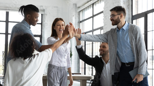 Excited successful multiracial business people with attractive mentor giving high five, celebrating win. Smiling diverse employees team engaged in team building activity at corporate meeting.