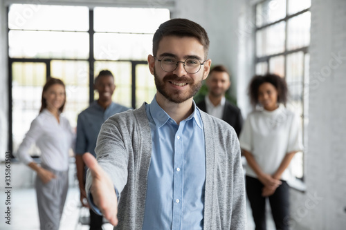 Close up headshot portrait of happy businessman shaking hand posture. Different smiling ethnicity businesspeople standing behind of male company chief. Leader of multi-ethnic team concept.