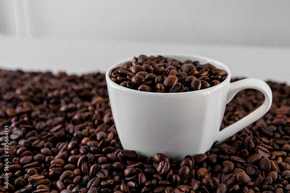 White mug with roasted coffee beans everywhere, inside the mug and a lot around it with white background. Great for going to a cafe, restaurant, cafeteria menu or as a sign. White mug with roasted coffee beans everywhere, inside the mug and a lot around it with white background. Great for going to a cafe, restaurant, cafeteria menu or as a sign.