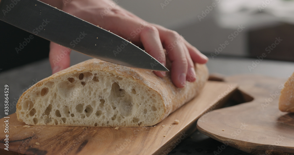 man slicing ciabatta with bread knife on olive board man slicing ciabatta with bread knife on olive board