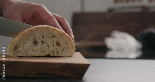 man slicing yesterday ciabatta with bread knife on olive board