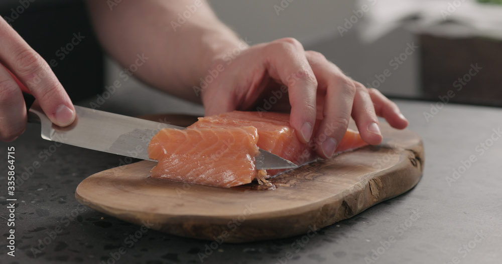 man hands slicing salted trout with knife on olive wood board