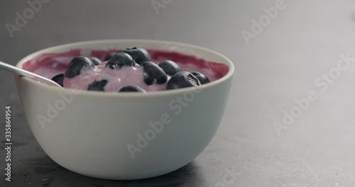 eat yogurt with blueberries from white bowl on concrete surface
