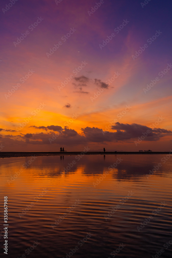 Burning bright sky during sunset on a tropical beach. Sunset during the exodus, the strength of people walking on water Burning bright sky during sunset on a tropical beach. Sunset during the exodus, the strength of people walking on water