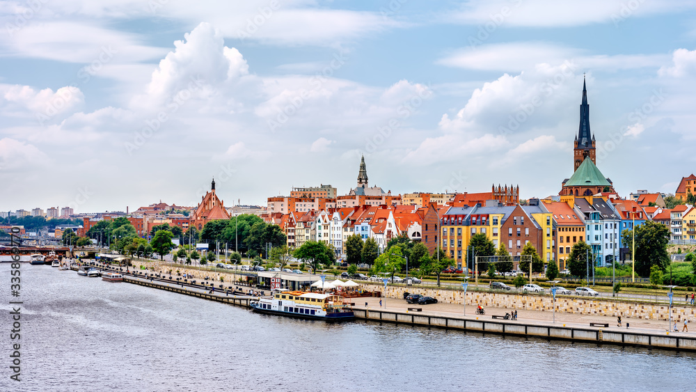 Ships anchored on Odra River pier. People relaxing on Piastowski Boulevard. Cathedral Basilica of St James the Apostle in background, Szczecin, Poland