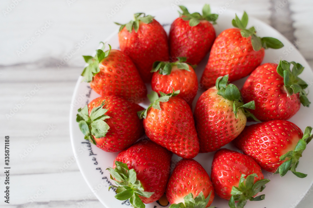 Fresh strawberries on a white plate on a soft wooden base Fresh strawberries on a white plate on a soft wooden base