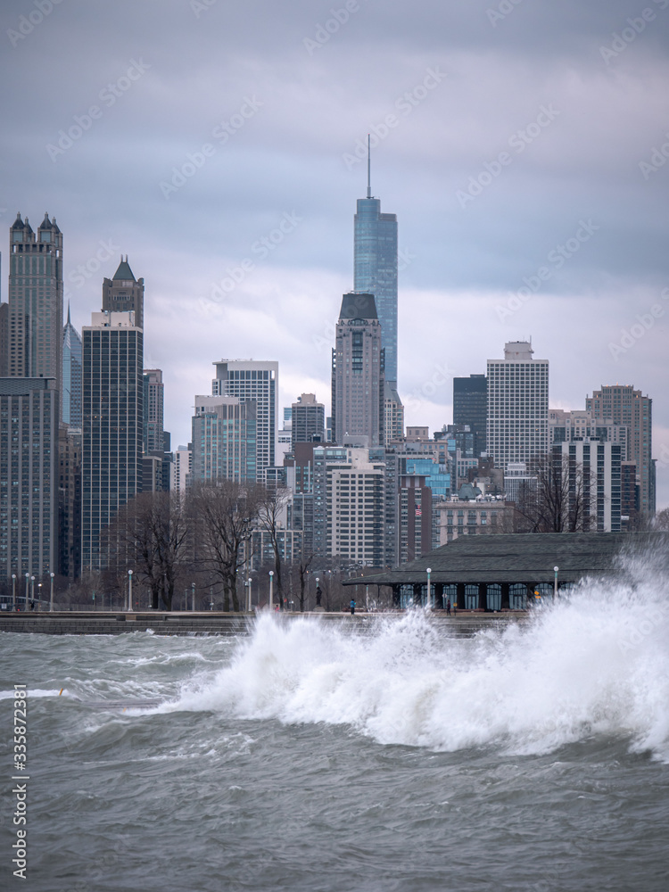 Chicago skyline view with waves crashing into the tiered shoreline and cascading back into the water during a windy evening and cloudy sunset pink and blue sky above.