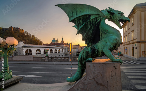 Dragon statue on Dragon bridge and Saint Nicholas Cathedral in background at sunset, Ljubljana, Slovenia