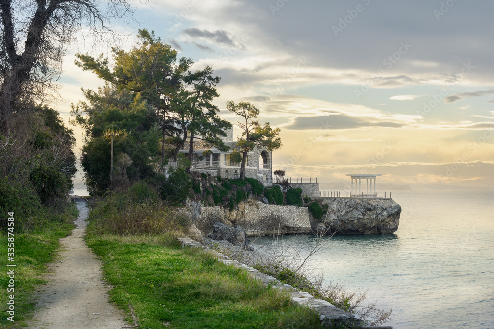 A path by the sea, ending in a seaside house. With clouds and trees and railway