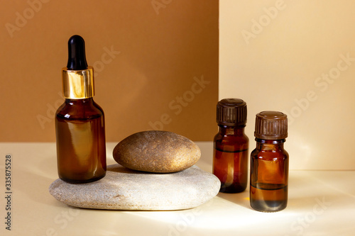 A glass cosmetic bottle with a dropper stands on a stone on a beige background with bright sunlight. Natural cosmetics concept, natural essential oil