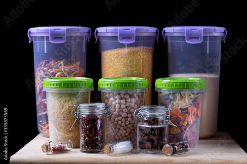 Assortment of groats and spices in plastic and glass jars on the wooden kitchen shelf. Concept of storage of non-perishable products